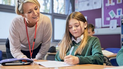 Teacher watching over school girl writing