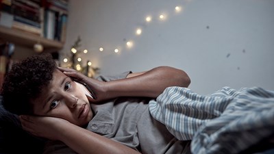 A concerned teenager on the phone in their bedroom with Christmas lights in the background.