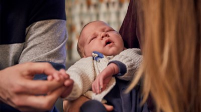 Father plays with the hand of his baby whilst mother holds baby in her arms