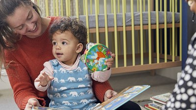 A parent smiling while reading a book with their baby.