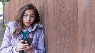 Young girl on phone outside next to a fence