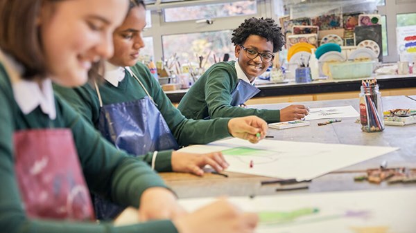 Children smiling and colouring with crayons in a classroom