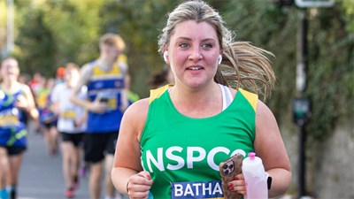 A woman in a green NSPCC vest running and smiling.