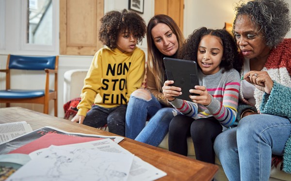 A family sat on a sofa looking at a computer tablet.