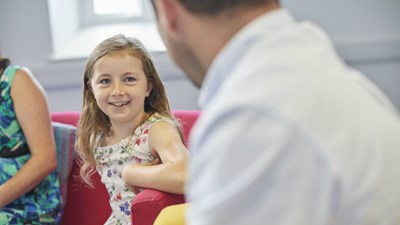 A young girl smiling while talking to an adult.