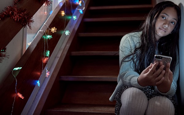 A child sat on a Christmas lit staircase while staring into the camera.