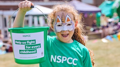 A young girl holds up an NSPCC fundraising bucket