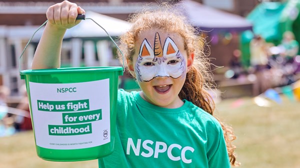 A young girl holds up an NSPCC fundraising bucket