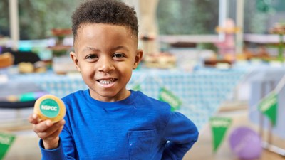 A young boy smiles and holds up a cupcake